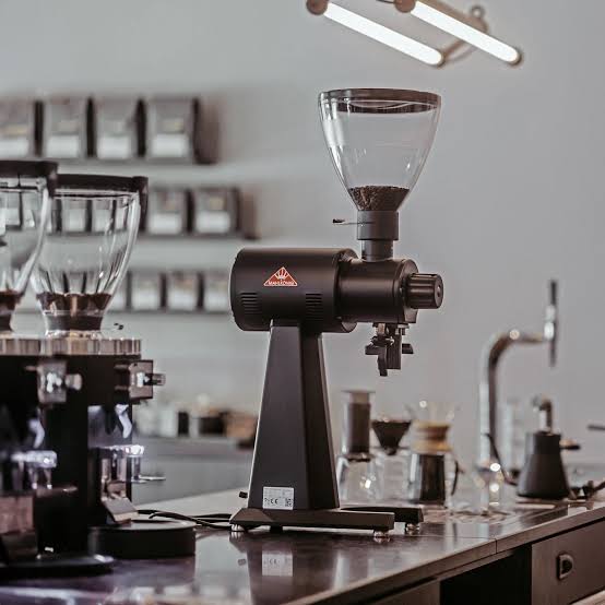 Molinillo de café profesional negro sobre un mostrador en una cafetería con fondo difuminado.